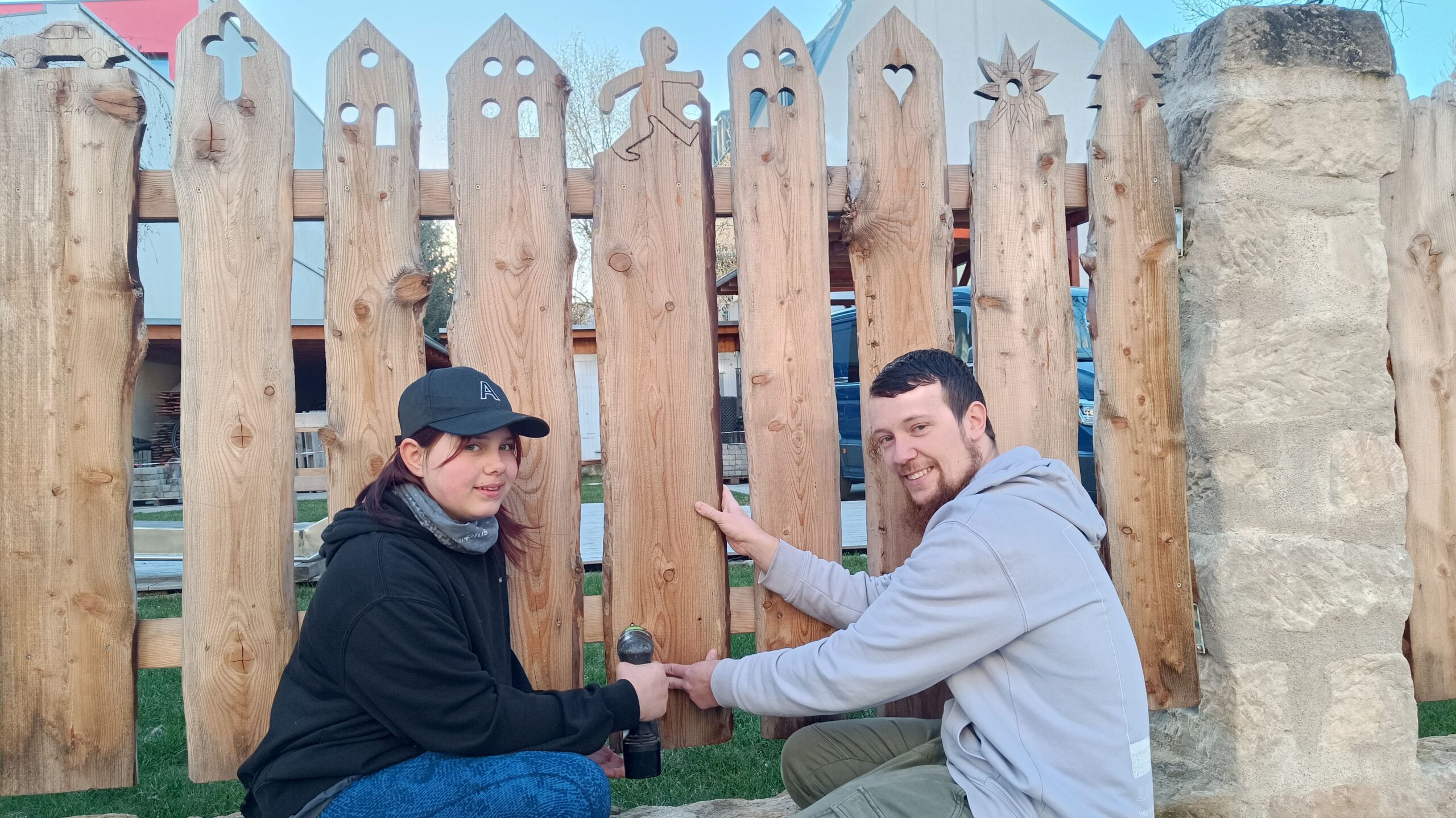 Sozialarbeiter Björn Wahlbuhl montiert mit einer Jugendlichen einen Holzzaun rund um den Spielplatz. 